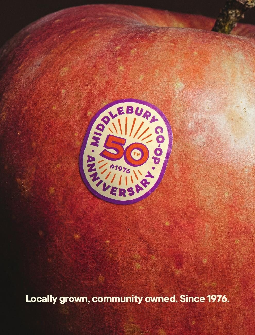 Awareness ad: a custom 50th-anniversary PLU sticker on an apple, with the line Locally grown, community owned. Since 1976.